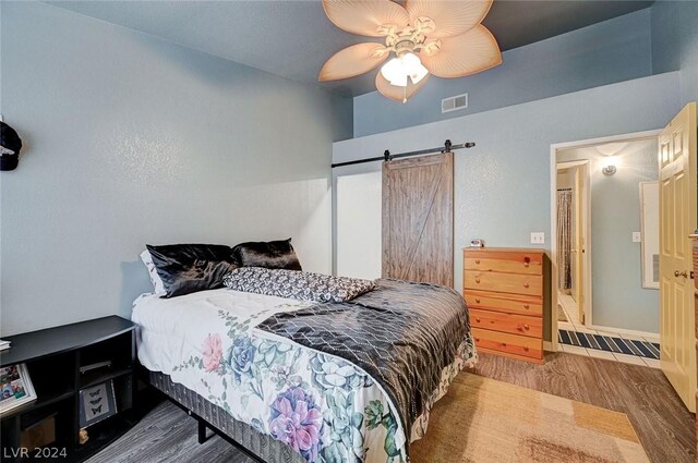 bedroom with a barn door, hardwood / wood-style floors, and ceiling fan