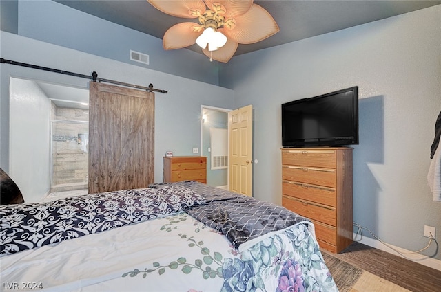 bedroom with ceiling fan, hardwood / wood-style flooring, ensuite bathroom, and a barn door