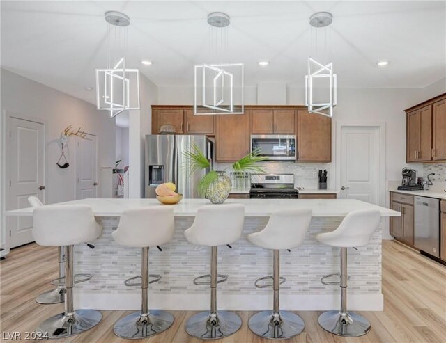 kitchen featuring light hardwood / wood-style floors, appliances with stainless steel finishes, decorative light fixtures, and a center island