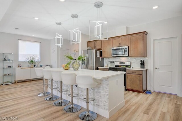 kitchen with pendant lighting, a breakfast bar area, decorative backsplash, light hardwood / wood-style floors, and stainless steel appliances