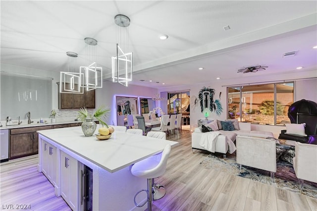 kitchen with sink, a breakfast bar, a kitchen island, decorative light fixtures, and light wood-type flooring