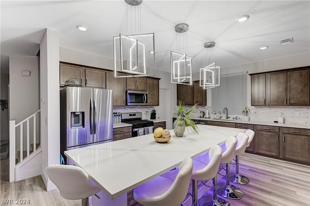 kitchen featuring stainless steel appliances, a kitchen island, hanging light fixtures, and dark brown cabinetry