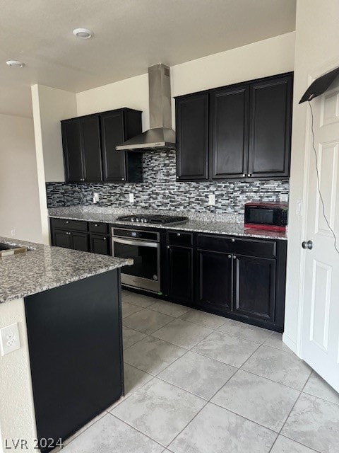 kitchen featuring tasteful backsplash, light stone counters, appliances with stainless steel finishes, and wall chimney range hood