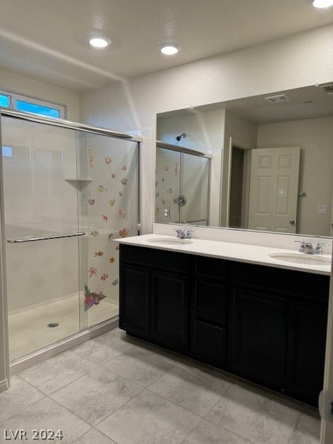 bathroom with a shower with shower door, dual bowl vanity, and tile patterned floors