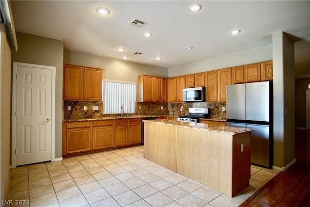 kitchen with stainless steel appliances, light stone countertops, a kitchen island, and light tile patterned floors