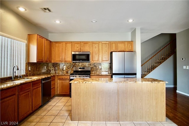 kitchen with sink, a center island, stainless steel appliances, light stone countertops, and backsplash