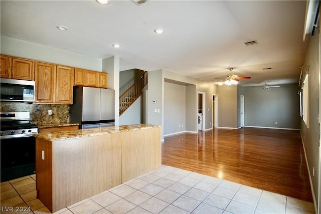 kitchen with light tile patterned flooring, appliances with stainless steel finishes, tasteful backsplash, a center island, and light stone countertops