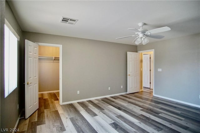 unfurnished bedroom featuring ceiling fan, multiple windows, wood-type flooring, a spacious closet, and a closet