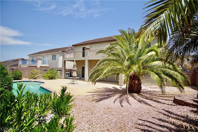 rear view of house with a fenced in pool, a patio, and a balcony