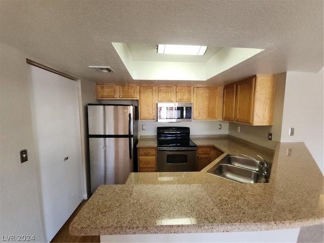 kitchen with sink, appliances with stainless steel finishes, a tray ceiling, kitchen peninsula, and light stone countertops