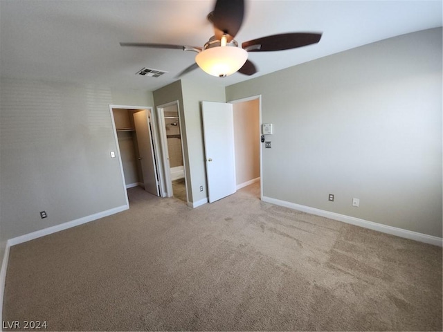 unfurnished bedroom featuring ensuite bath, a spacious closet, light carpet, a closet, and ceiling fan