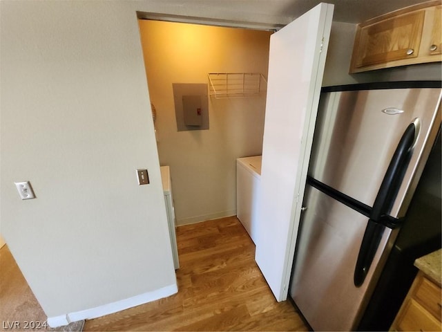 kitchen featuring light hardwood / wood-style flooring, stainless steel refrigerator, electric panel, washer / dryer, and light brown cabinets