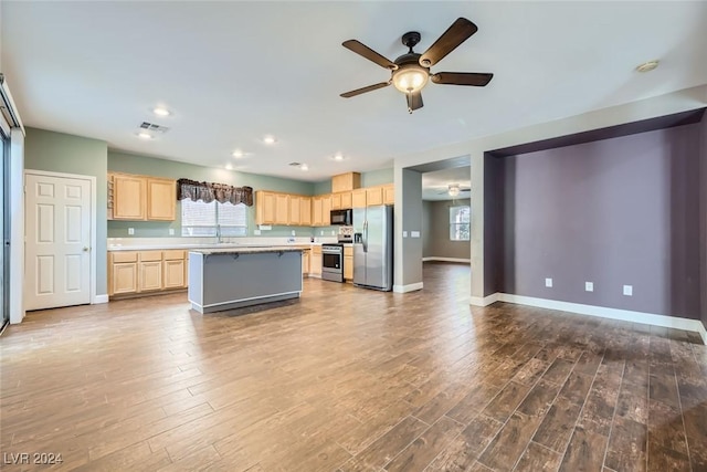 kitchen with a kitchen island, appliances with stainless steel finishes, wood-type flooring, ceiling fan, and light brown cabinets