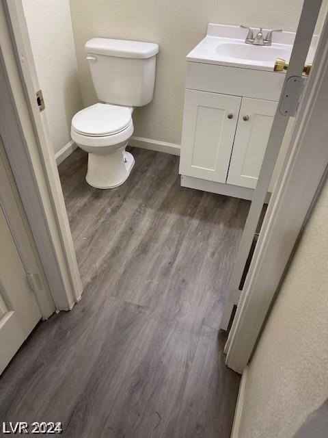 half bath featuring baseboards, toilet, wood finished floors, and vanity