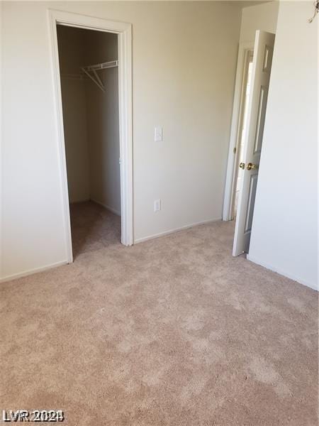 unfurnished bedroom featuring a walk in closet, light colored carpet, and a closet