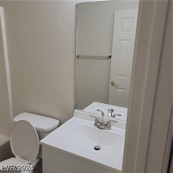 bathroom with vanity, a shower, toilet, a textured wall, and a washtub