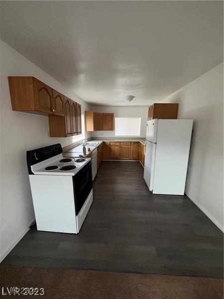 kitchen with light countertops, white appliances, brown cabinetry, and baseboards