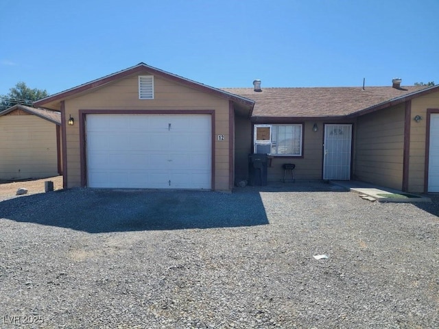 ranch-style home featuring an attached garage, a shingled roof, and gravel driveway