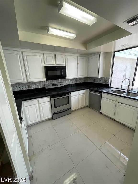 kitchen featuring sink, light tile patterned floors, appliances with stainless steel finishes, a raised ceiling, and white cabinets