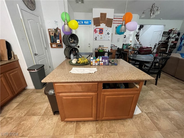 kitchen featuring light tile patterned flooring, brown cabinets, decorative light fixtures, and a center island