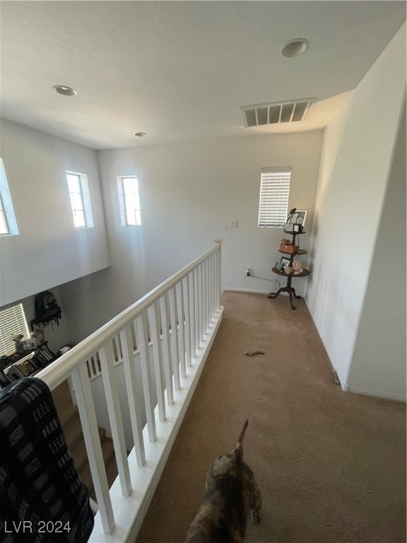 hall with visible vents, light carpet, and an upstairs landing