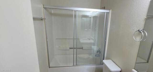 bathroom featuring toilet and shower / bath combination with glass door