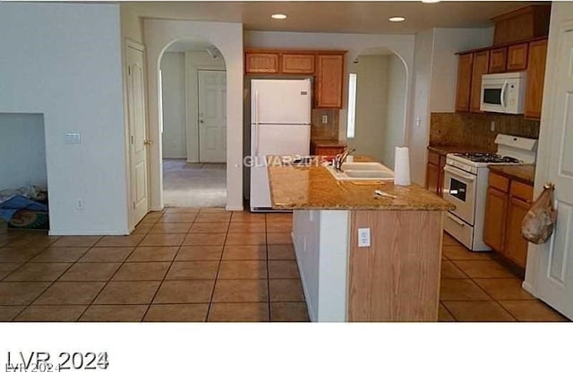 kitchen featuring light tile patterned flooring, white appliances, light stone counters, sink, and a center island with sink