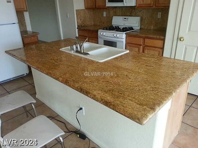 kitchen with white appliances, sink, backsplash, light tile patterned floors, and an island with sink