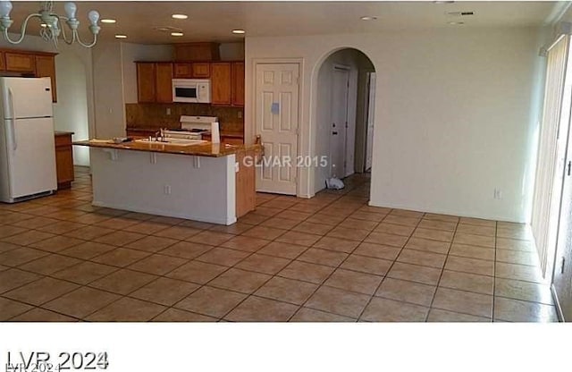 kitchen with tasteful backsplash, light tile patterned floors, white appliances, a chandelier, and a kitchen island with sink