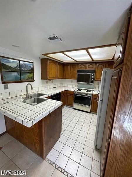 kitchen with sink, white appliances, light tile patterned flooring, tile countertops, and kitchen peninsula