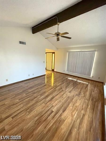 empty room with hardwood / wood-style flooring, a textured ceiling, and lofted ceiling with beams