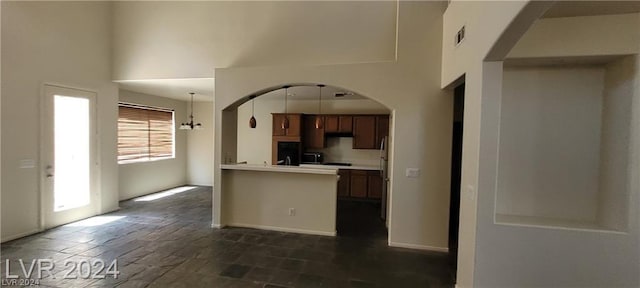 kitchen with hanging light fixtures, a towering ceiling, kitchen peninsula, and stainless steel refrigerator