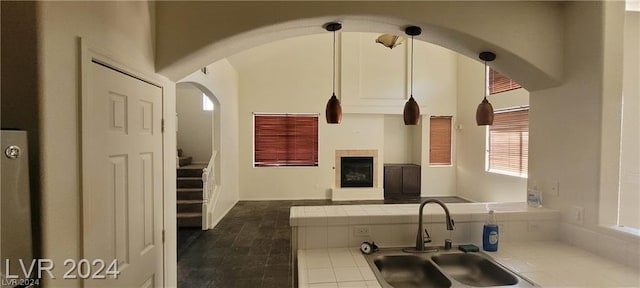 kitchen featuring a tiled fireplace, sink, decorative light fixtures, and tile countertops