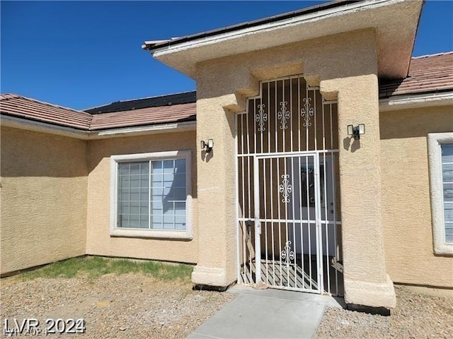 entrance to property featuring stucco siding, solar panels, and a gate