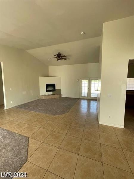 unfurnished living room with tile patterned floors, a fireplace with raised hearth, a ceiling fan, baseboards, and vaulted ceiling