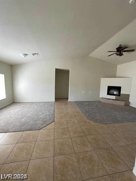 unfurnished living room with a tiled fireplace, tile patterned flooring, carpet floors, and ceiling fan