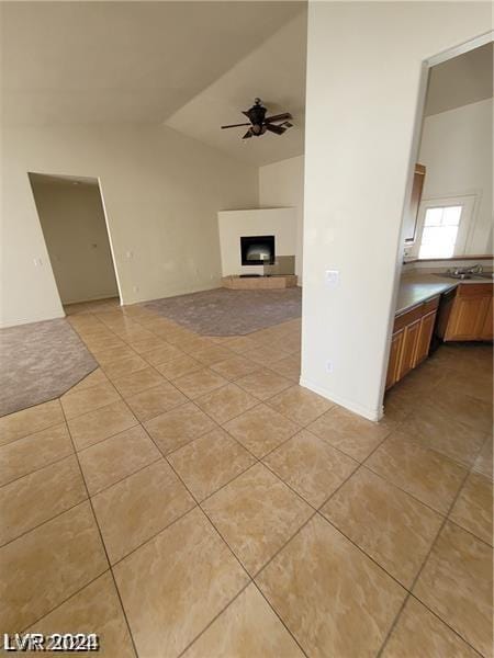 unfurnished living room with light tile patterned floors, a fireplace with raised hearth, ceiling fan, and vaulted ceiling