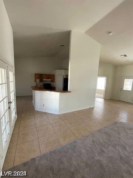 kitchen with dark countertops, open floor plan, lofted ceiling, light tile patterned floors, and fridge