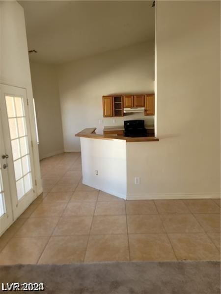 kitchen with electric range, brown cabinets, high vaulted ceiling, under cabinet range hood, and light tile patterned floors