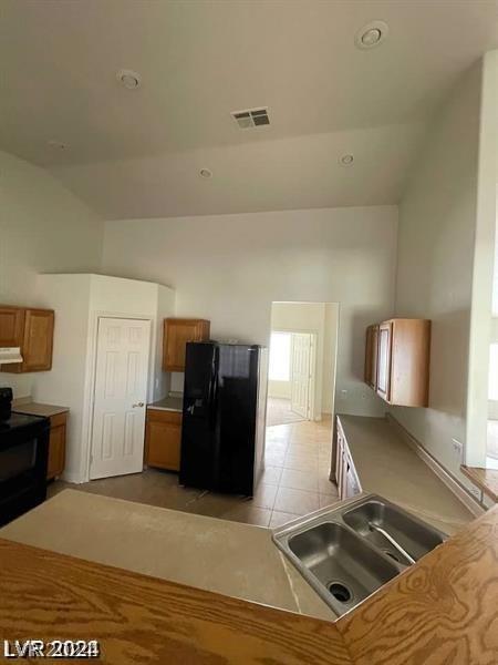 kitchen with light tile patterned floors, brown cabinetry, visible vents, a sink, and black appliances