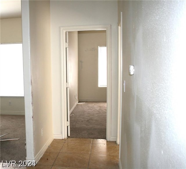 corridor featuring tile patterned floors, carpet flooring, and baseboards