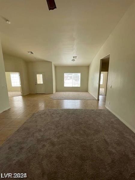 empty room featuring light carpet, plenty of natural light, light tile patterned flooring, and vaulted ceiling