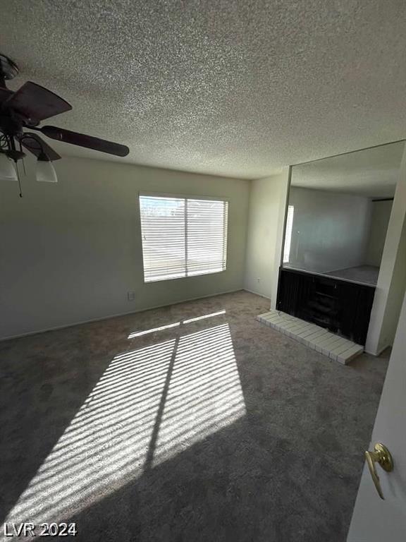 unfurnished living room featuring ceiling fan, a textured ceiling, and dark colored carpet