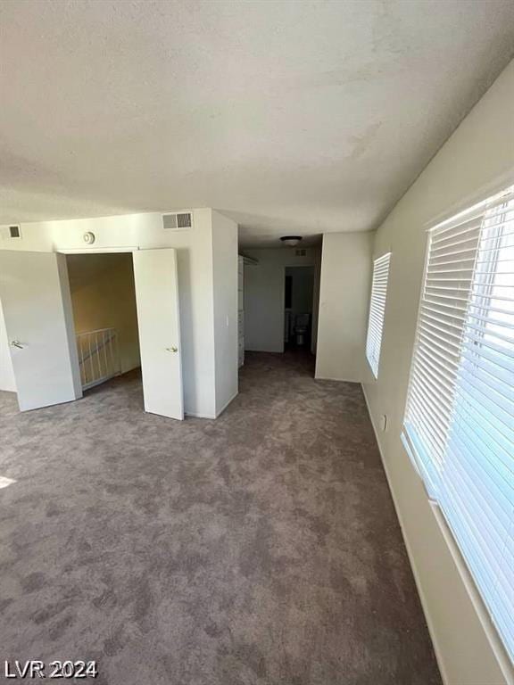 unfurnished living room featuring a textured ceiling and dark carpet