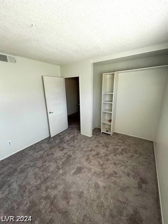 unfurnished bedroom with a textured ceiling, dark carpet, and a closet