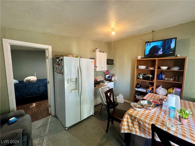 kitchen featuring white fridge with ice dispenser, white cabinets, concrete floors, and a textured ceiling