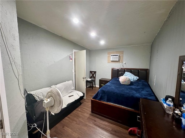 bedroom with a textured wall, a wall mounted air conditioner, and wood finished floors