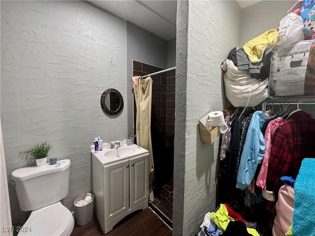 bathroom with a textured wall, toilet, wood finished floors, a tile shower, and vanity