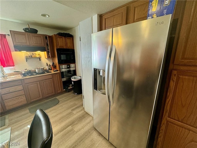 kitchen featuring brown cabinets, stainless steel appliances, light countertops, light wood-style flooring, and under cabinet range hood