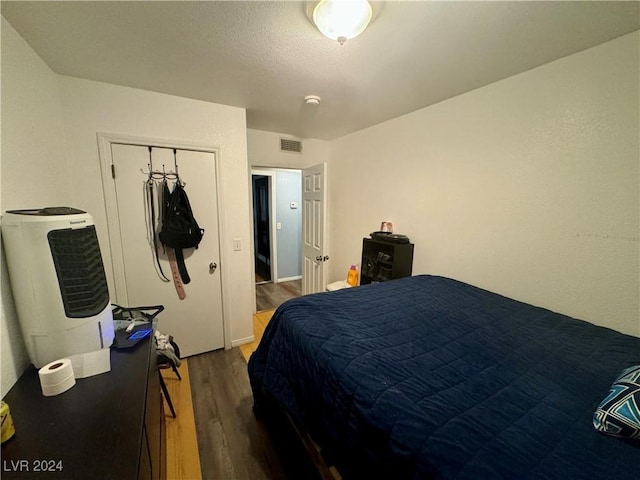 bedroom featuring a textured ceiling, visible vents, dark wood finished floors, and a closet